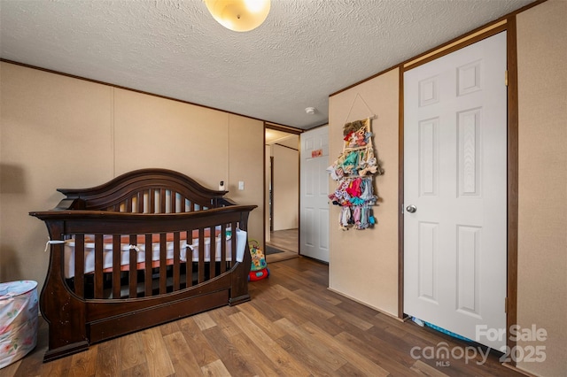 bedroom with a crib, a textured ceiling, and wood finished floors