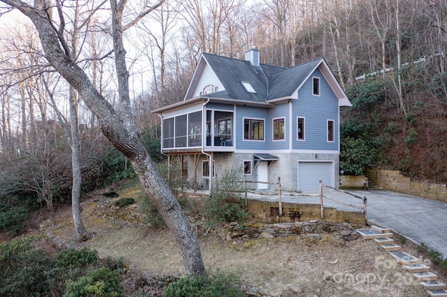 view of front facade featuring an attached garage, a sunroom, a chimney, and concrete driveway