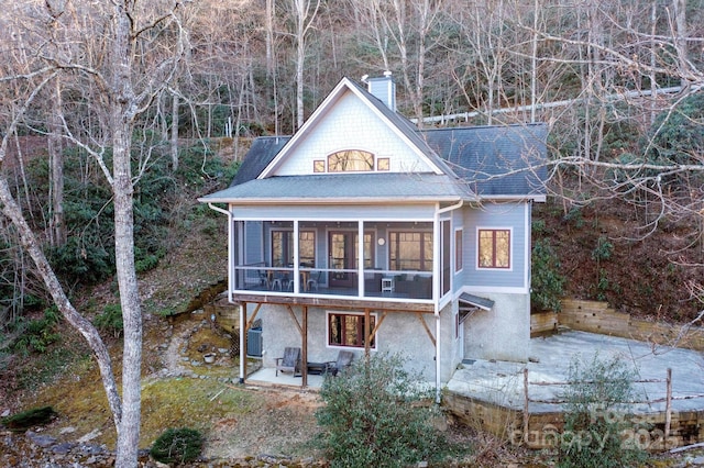 rear view of house with a patio, central AC unit, a sunroom, roof with shingles, and a chimney