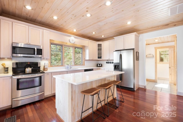 kitchen featuring glass insert cabinets, appliances with stainless steel finishes, a breakfast bar area, light countertops, and a sink