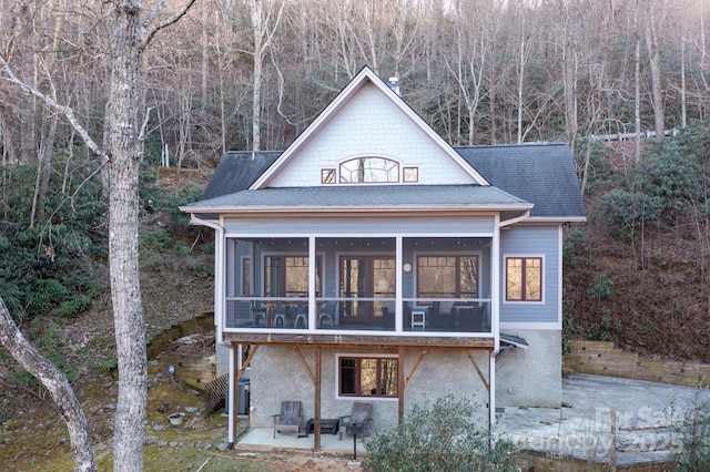 back of property featuring a shingled roof, a sunroom, a patio area, and a chimney