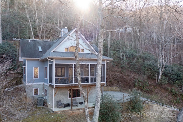 back of property with a patio, a chimney, a shingled roof, a sunroom, and cooling unit