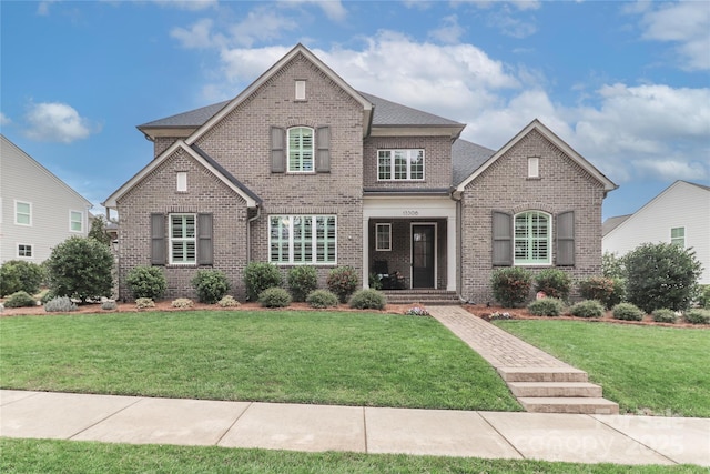 view of front of home with brick siding, a front lawn, and a shingled roof