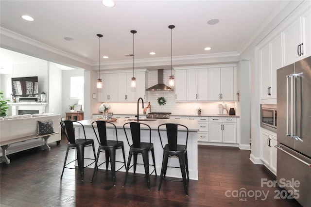 kitchen featuring a breakfast bar, dark wood-style flooring, ornamental molding, stainless steel appliances, and wall chimney range hood