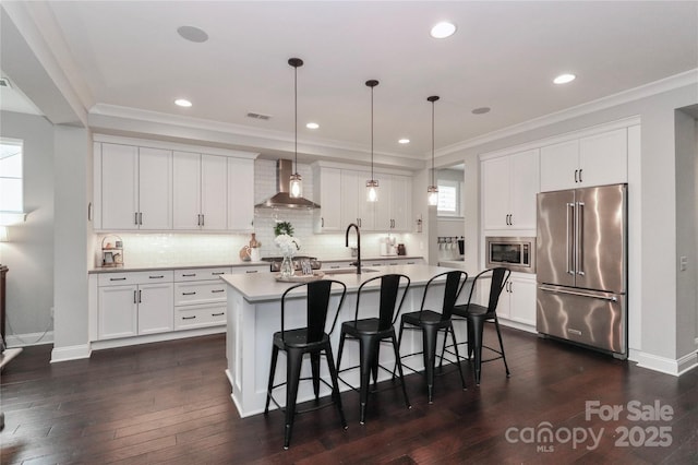 kitchen with stainless steel appliances, an island with sink, wall chimney exhaust hood, and ornamental molding