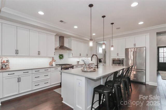 kitchen featuring visible vents, a sink, appliances with stainless steel finishes, crown molding, and wall chimney range hood