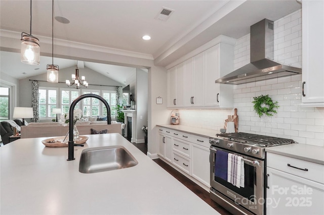 kitchen featuring visible vents, stainless steel range with gas stovetop, a sink, light countertops, and wall chimney exhaust hood