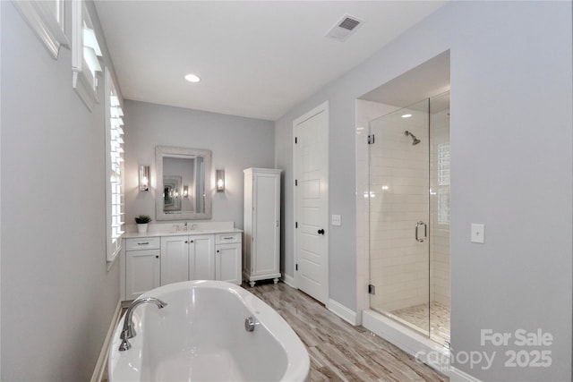 bathroom featuring visible vents, a tub to relax in, a stall shower, wood finished floors, and vanity