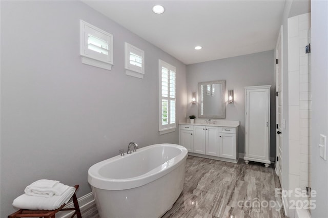 full bath with a freestanding bath, vanity, baseboards, and wood finished floors