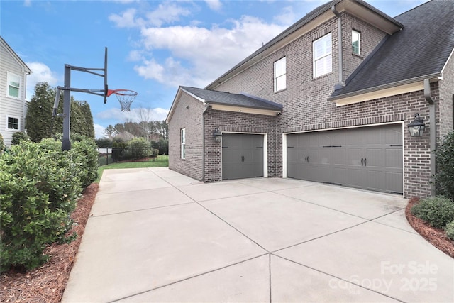 view of side of home featuring concrete driveway, brick siding, and roof with shingles