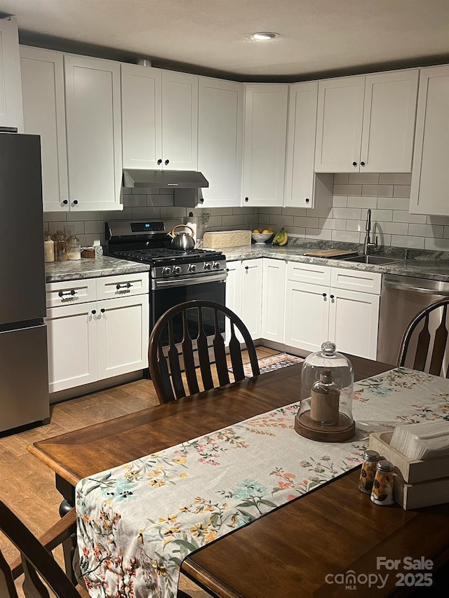 kitchen featuring dark wood-style floors, stainless steel appliances, decorative backsplash, and under cabinet range hood