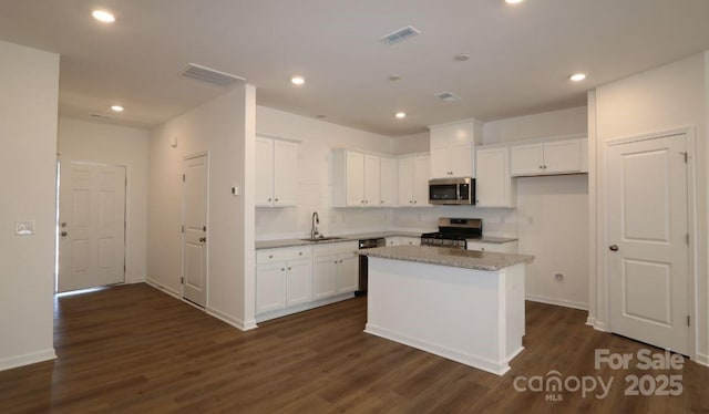 kitchen featuring dark wood-style flooring, stainless steel appliances, visible vents, white cabinets, and a sink