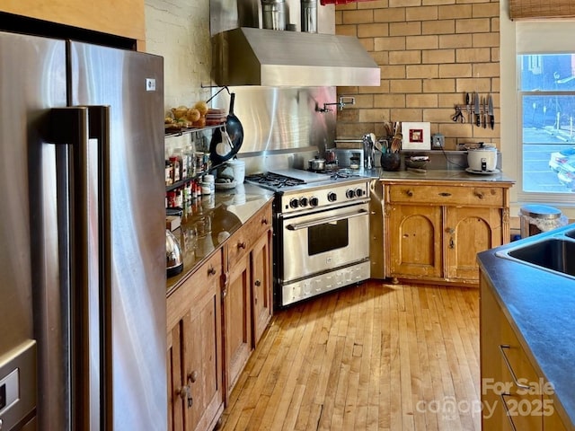 kitchen with light wood-style flooring, backsplash, appliances with stainless steel finishes, exhaust hood, and brown cabinetry