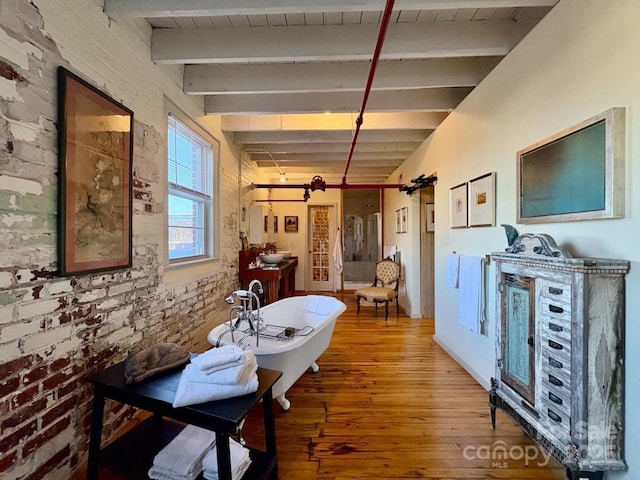 dining area featuring beam ceiling, brick wall, and wood finished floors