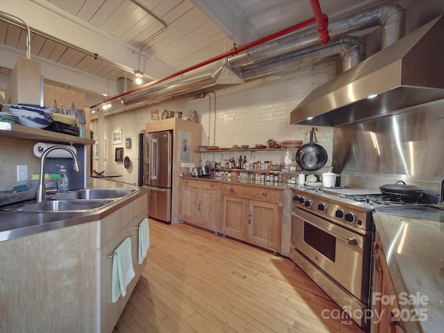 kitchen with beamed ceiling, light wood-style flooring, stainless steel appliances, wall chimney exhaust hood, and a sink