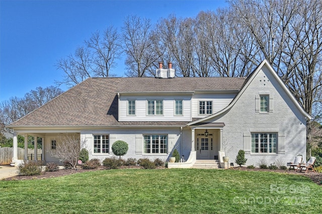 view of front facade with roof with shingles, a front yard, and brick siding