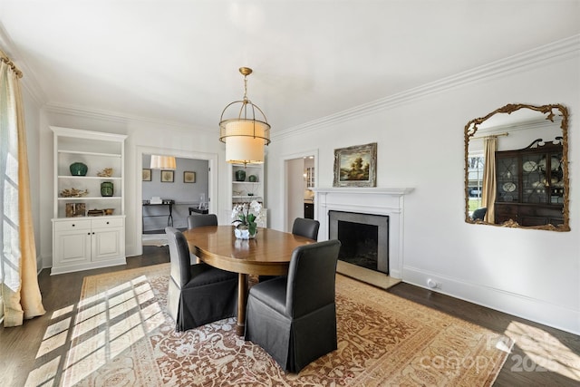 dining area featuring a fireplace with raised hearth, crown molding, baseboards, and wood finished floors