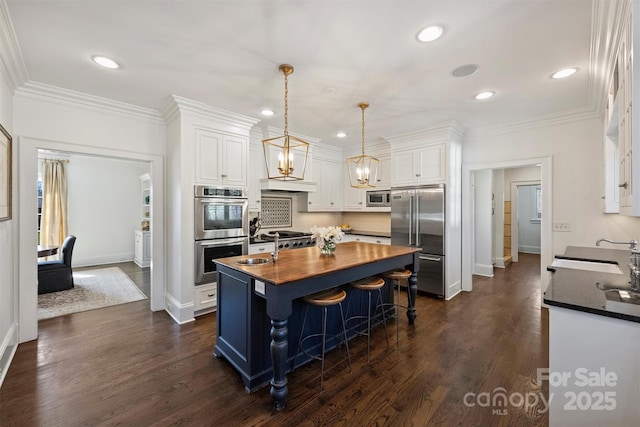 kitchen with built in appliances, a sink, white cabinetry, wooden counters, and ornamental molding