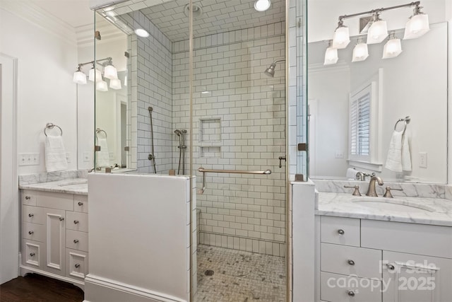 bathroom with a shower stall, crown molding, two vanities, and a sink