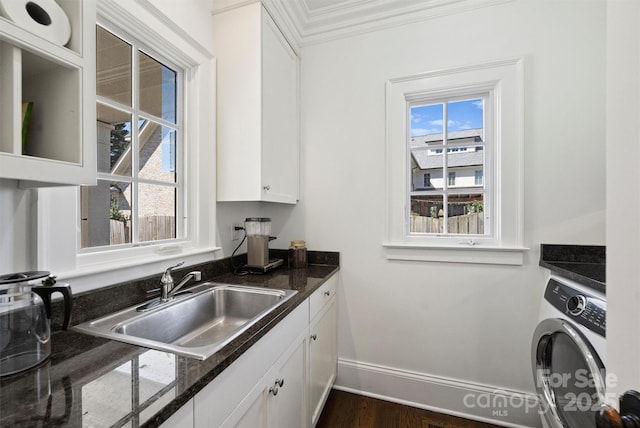 kitchen featuring washer / dryer, ornamental molding, dark stone countertops, white cabinetry, and a sink