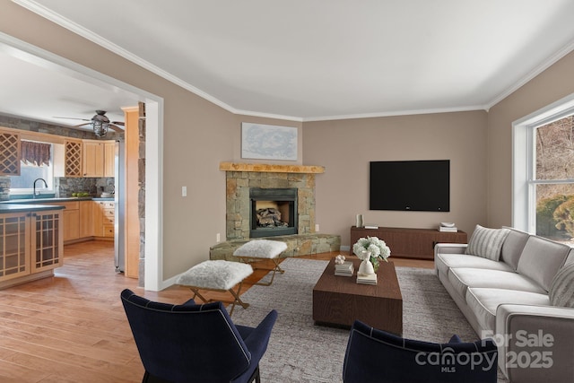 living room with baseboards, light wood-style flooring, ceiling fan, ornamental molding, and a fireplace