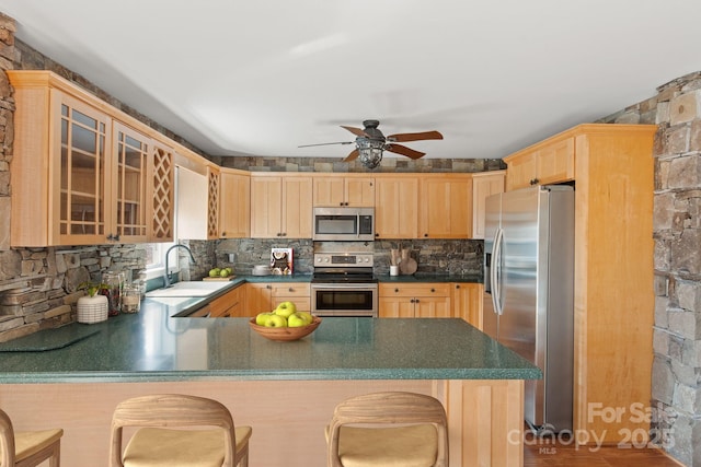 kitchen featuring glass insert cabinets, backsplash, stainless steel appliances, light brown cabinetry, and a sink