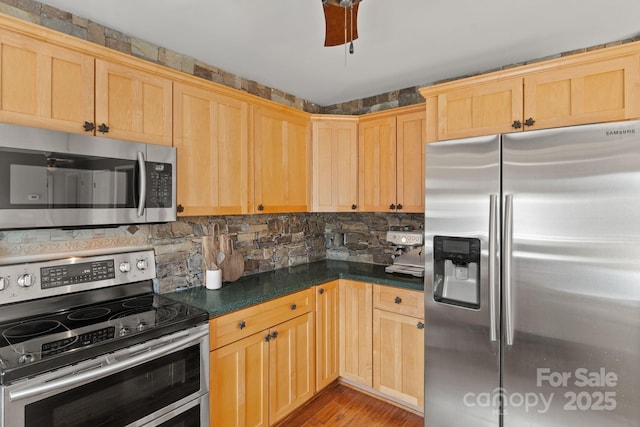 kitchen featuring stainless steel appliances, dark countertops, light brown cabinets, and tasteful backsplash