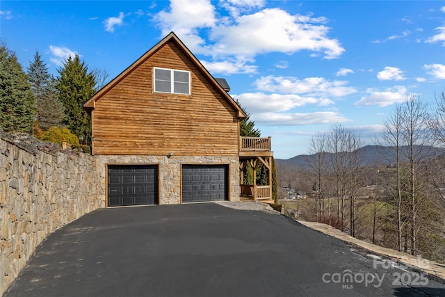 view of side of home with stone siding, driveway, a deck with mountain view, and an attached garage