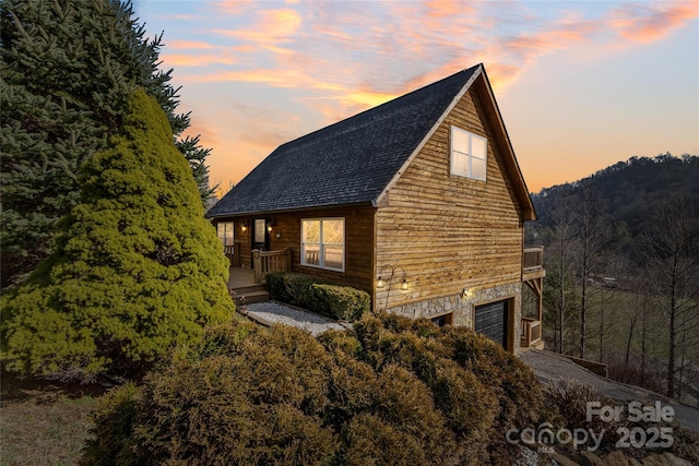 property exterior at dusk featuring a garage and roof with shingles