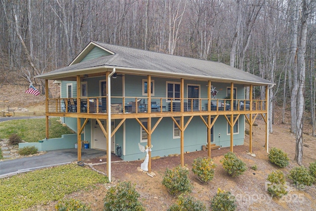 view of front of property with a garage, driveway, a shingled roof, and a view of trees