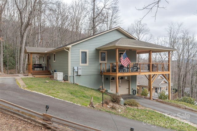 view of front of house featuring a shingled roof, aphalt driveway, an attached garage, covered porch, and a front yard