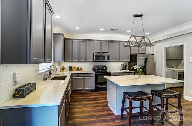 kitchen featuring dark wood finished floors, appliances with stainless steel finishes, washing machine and clothes dryer, a kitchen bar, and a sink