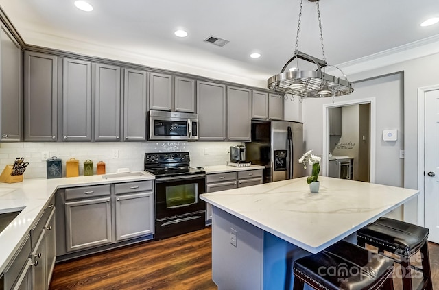 kitchen featuring a breakfast bar area, stainless steel appliances, visible vents, backsplash, and dark wood-type flooring