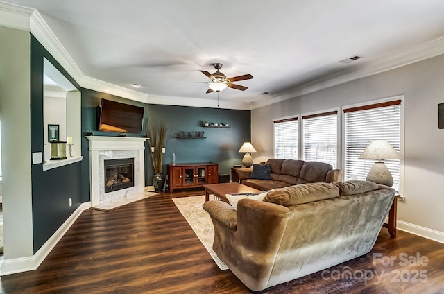 living area with baseboards, ceiling fan, ornamental molding, wood finished floors, and a high end fireplace