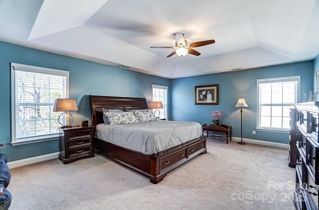 bedroom featuring light colored carpet, a tray ceiling, multiple windows, and baseboards