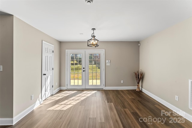 unfurnished dining area featuring visible vents, wood finished floors, baseboards, a chandelier, and french doors