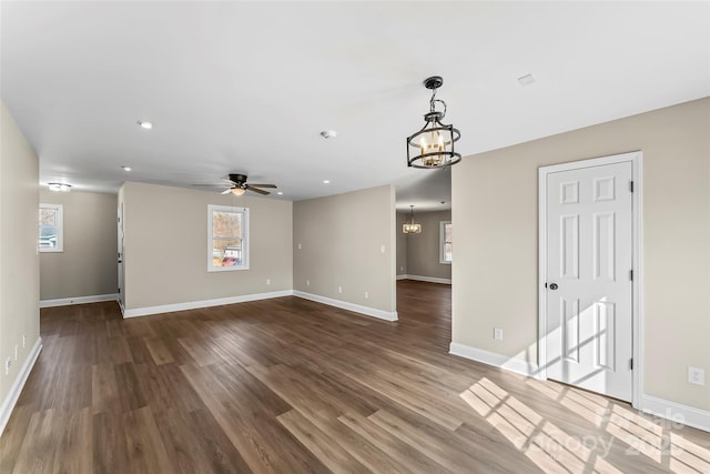 unfurnished living room featuring baseboards, ceiling fan with notable chandelier, and wood finished floors