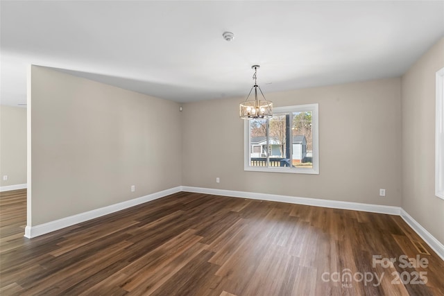 spare room with baseboards, a chandelier, and dark wood-type flooring