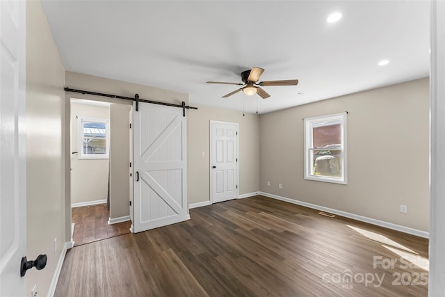unfurnished bedroom with a barn door, baseboards, ceiling fan, and wood finished floors