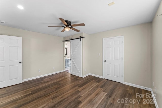 unfurnished bedroom featuring baseboards, a barn door, and wood finished floors
