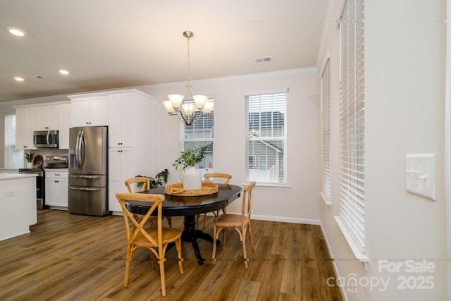 dining area featuring dark wood-type flooring, a chandelier, visible vents, and ornamental molding