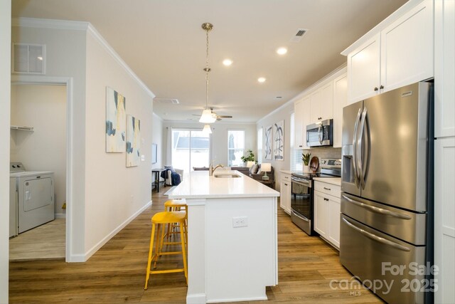 kitchen with stainless steel appliances, a sink, visible vents, ornamental molding, and an island with sink