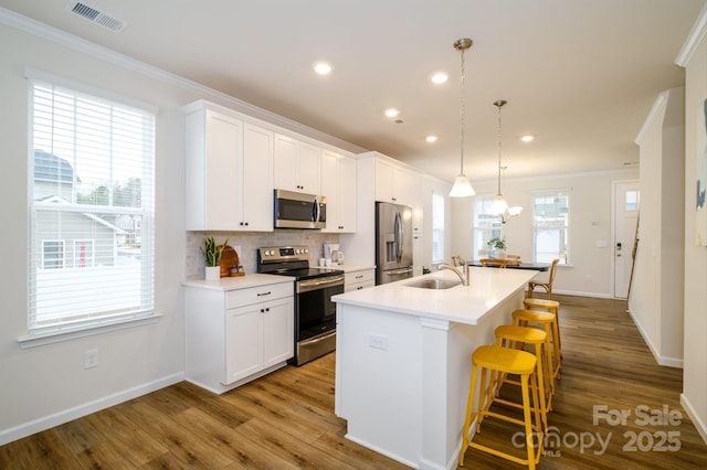 kitchen featuring a center island with sink, visible vents, appliances with stainless steel finishes, ornamental molding, and a kitchen breakfast bar