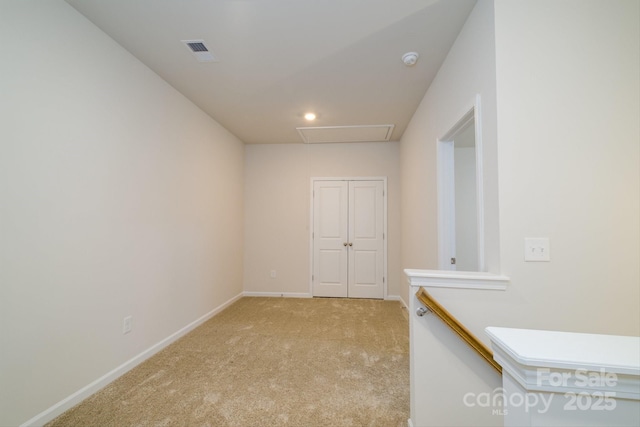 empty room with attic access, visible vents, baseboards, and light colored carpet