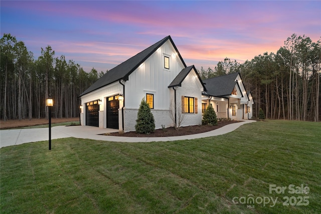 view of front of house featuring a garage, a lawn, concrete driveway, board and batten siding, and brick siding