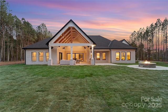 back of property at dusk with a patio area, an outdoor living space with a fire pit, a yard, and brick siding