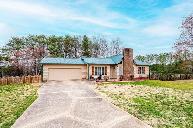 view of front of house with driveway, a front yard, an attached garage, metal roof, and a chimney