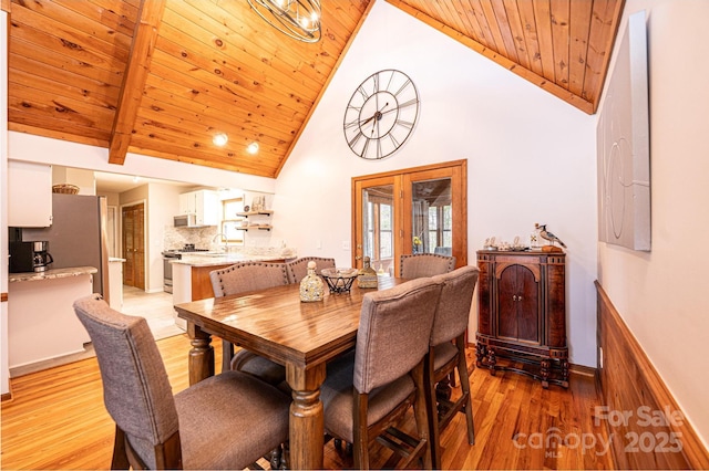 dining area featuring baseboards, beam ceiling, wooden ceiling, light wood-style floors, and high vaulted ceiling