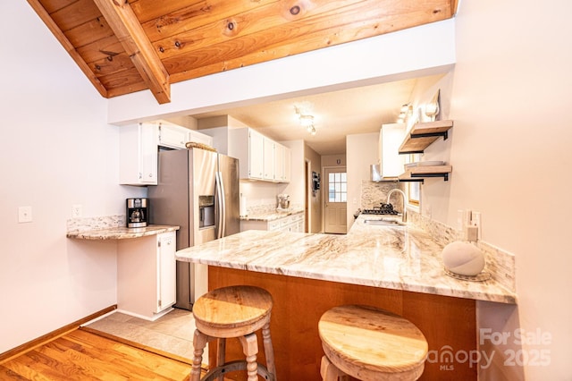 kitchen with a peninsula, light wood-style flooring, stainless steel fridge with ice dispenser, a sink, and white cabinetry