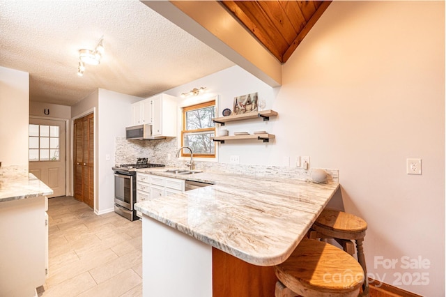 kitchen featuring a sink, white cabinetry, appliances with stainless steel finishes, a breakfast bar area, and a peninsula